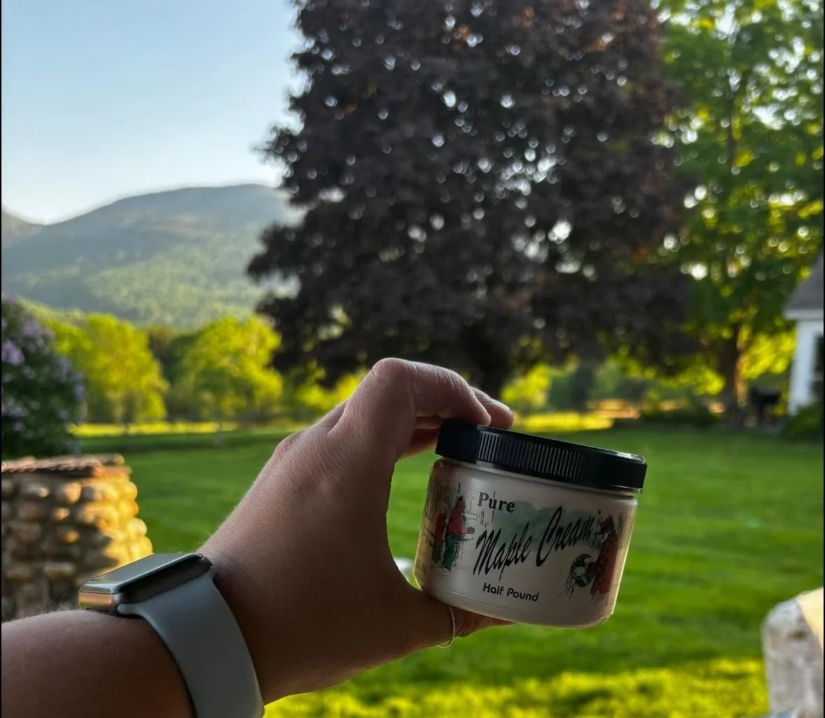 A jar of maple cream held up against a Vermont mountain view